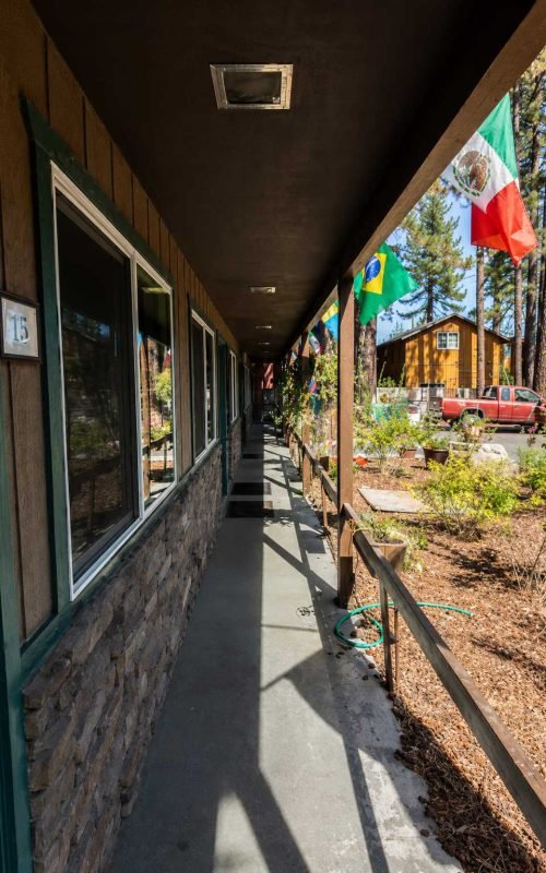 Covered walkway outside the Alder Inn guest rooms, decorated with international flags and overlooking a wooded garden.
